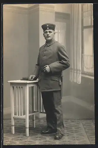 Foto-AK Soldat in Feldgrau Uniform mit Bajonett vor einer Studiokulisse
