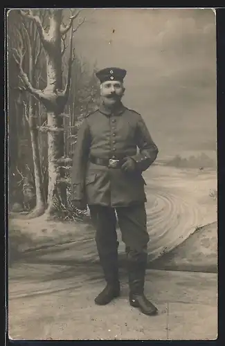 Foto-AK älterer Soldat in Feldgrau Uniform mit Mustasch vor einer Winter Studiokulisse