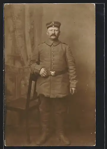 Foto-AK Soldat in Feldgrau Uniform mit Krätzchen und Mustasch