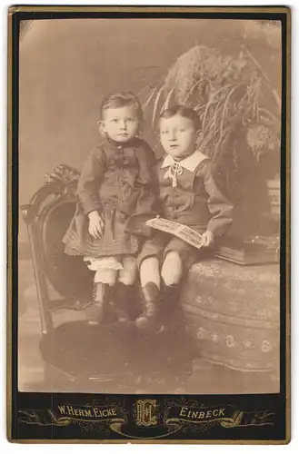 Fotografie W. Herm. Eicke, Einbeck, Portrait Kinderpaar in hübscher Kleidung mit Bilderbuch