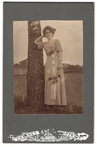 Fotografie Cabinet Portrait, Ort unbekannt, Portrait bürgerliche Dame mit Blumen an Baum gelehnt
