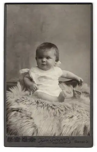 Fotografie Karl Schipper, Wiesbaden, Rheinstrasse 31, Portrait niedliches Kleinkind im weissen Hemd auf Fell sitzend