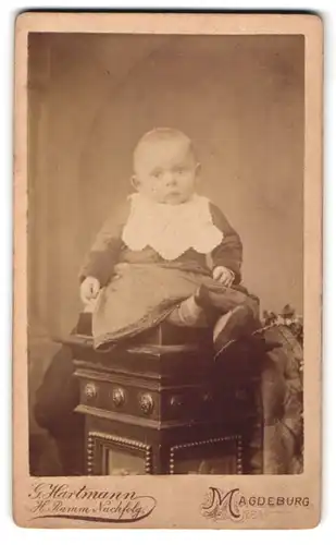 Fotografie G. Hartmann, Magdeburg, Lüneburgerstrasse 2, Portrait niedliches Kleinkind im Kleid auf Sockel sitzend