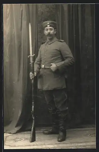 Foto-AK Soldat in Feldgrau Uniform mit Krätzchen und Sägebajonett auf Gewehr
