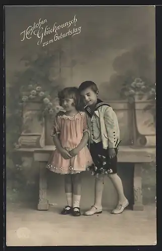Foto-AK R & K / L Nr. 8819/2: Junge und Mädchen stehen vor einer Bank, Herzlichen Glückwunsch zum Geburtstag
