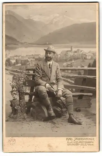 Fotografie Karl Jagerspacher, Zell am See, Herr in Wanderschuhen mit Stock und Hut vor einer Studiokulisse der Stadt