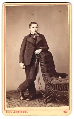 Fotografie Klotz & Hentschel, Hof, junger Mann im Anzug mit Fliege am Sessel lehnend