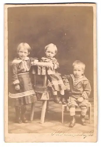 Fotografie unbekannter Fotograf und Ort, drei niedliche kleine Kinder in Kleidern und Matrosenanzug