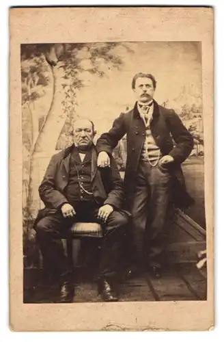 Fotografie unbekannter Fotograf und Ort, zwei Herren in Anzügen mit Ketten vor einer Studiokulisse