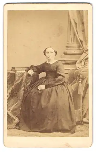Fotografie H. Mathaus, München, junge Frau im dunklen Kleid sitzt am Rand eines Sessels