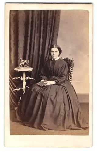 Fotografie unbekannter Fotograf und Ort, junge Frau im dunklen Kleid sitzend im Atelier, Pferde Bronze auf dem Tisch