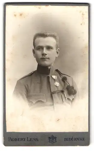 Fotografie Robert Lenk, Budweis, K.u.K. Soldat in Uniform mit Orden und Schützenschnur, Pfeife