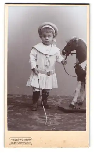 Fotografie Atelier Wertheim, Berlin, kleines Kind im weissen Kleid mit Schaukelpferd auf Rädern