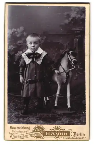 Fotografie Adolf Haynn, Berlin, junger Knabe im Kleid mit seinem Schaukelpferd