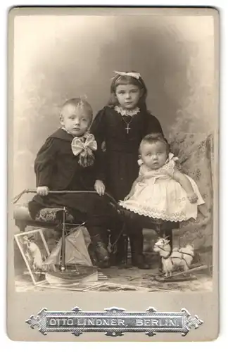 Fotografie Otto Lindner, Berlin, drei kleine Kinder mit Ziegengespann und Segelbott am Boden, Spielzeug