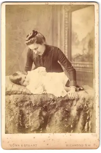 Fotografie Gunn & Stuart, Richmond, junge Mutter beugt sich über ihre Tochter auf Pelzdecken