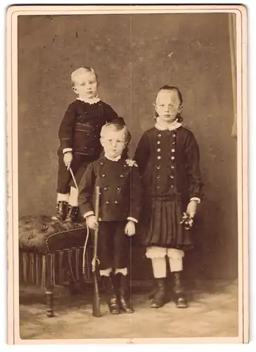 Fotografie unbekannter Fotograf und Ort, drei junge Kinder mit Spielzeug Gewehr und Peitsche