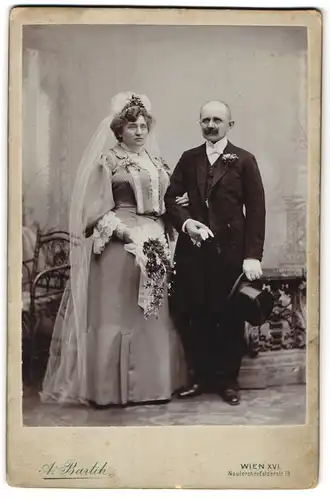 Fotografie A. Bartik, Wien, Braut und Bräutigam im Hochzeitskleid und Anzug mit Zylinder und Brautstrauss