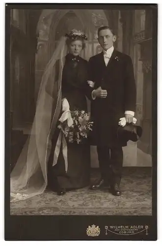 Fotografie Wilhelm Adler, Coburg, junges Brautpaar im schwarzen Hochzeitskleid und im Anzug mit Zylinder, Studokulisse