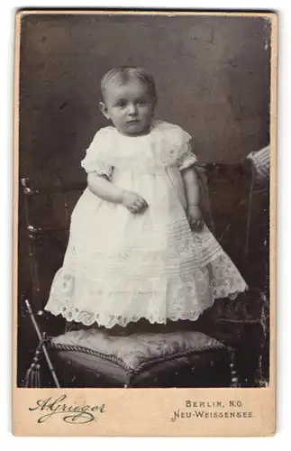 Fotografie A. Grieger, Berlin Neu-Weissensee, Süsses Kleinkind mit Mittelscheitel im Rüschenkleid