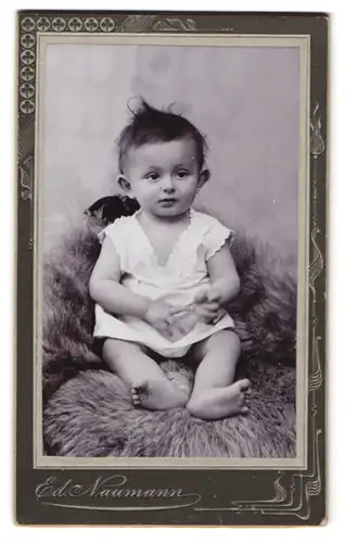 Fotografie Ed. Naumann, Meerane i. Sa., Augustus-Str. 33, Putziges Baby im Strampelkleid auf einem Fell