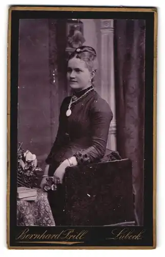 Fotografie Berhard Prill, Lübeck, Breite Strasse 35, Junge Dame mit Halskette und Haarschmuck lehnt an Stuhl
