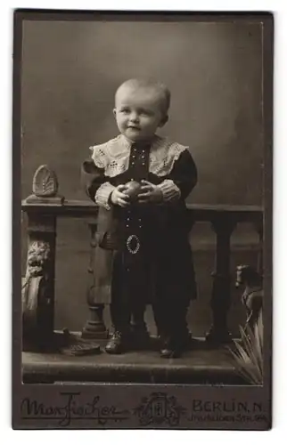 Fotografie Max Fischer, Berlin, Invaliden Str. 164, Süsser Junge im schwarzen Kleid mit Ball und Spielzeugpferd