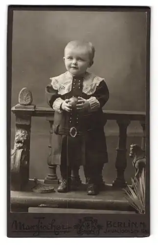 Fotografie Max Fischer, Berlin, Invalidenstr. 164, Süsser Junge im schwarzen Kleid mit Ball in der Hand schaut belustigt