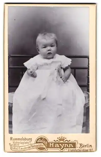 Fotografie Adolf Haynn, Berlin, Frankfurter Allee 197, Niedliches Kleinkind im langen weissen Kleid schaut müde drein