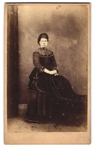 Fotografie George and Smith, London, Military Road 16, Dame im schwarzen Kleid mit Hut lehnt erbost an einem Stuhl