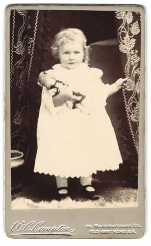 Fotografie W. C. Compton, London, 69, Marlborough Rd., Süsses blondes Mädchen mit Puppe im Arm