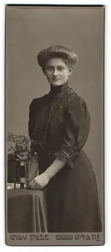 Fotografie Willy Dose, Bremen, Wall 117, Junge schöne Dame im schwarzen eleganten Kleid mit Perlenkette nebst Tisch