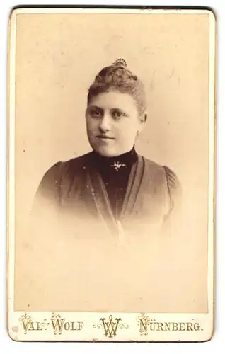 Fotografie Val. Wolf, Nürnberg, Breitegasse 97, Junge Dame im schwarzen Kleid mit Brosche und seichtem Lächeln