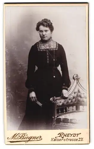 Fotografie M. Biegner, Rheydt, Kaiserstr. 27, Bürgerliche Dame im schwarzen Kleid mit Buch und Kette nebst Stuhl