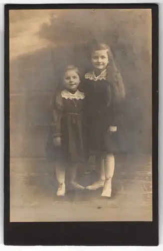 Fotografie Fuchs & Co., Berlin-Charlottenburg, zwei niedliche kleine Mädchen mit offenen Haaren in dunklen Kleidern