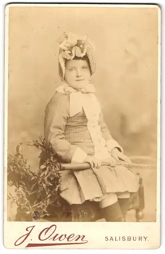 Fotografie J. OWen, Salisbury, hübschens kleines englisches Mädchen im Sommerkleid mit Haube und Tennisschläger