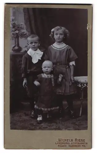 Fotografie Wilhelm Riege, Lüneburg, Stintmarkt 16, Junger Bursche im Hemd mit Geschwisterpaar in dunklen Kleidern