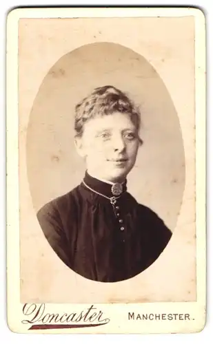 Fotografie E. Doncaster, Manchester, Oxford St. 75, Junge Dame im schwarzen Kleid mit Brosche und Kreuzkette am Lächeln
