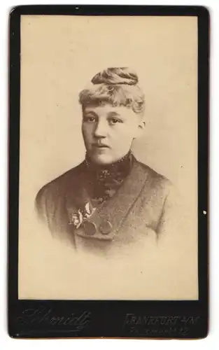 Fotografie J. Schmidt, Frankfurt a. M., Junge hübsche Dame im dunklen Mantel mit Rosen und Blumebrosche