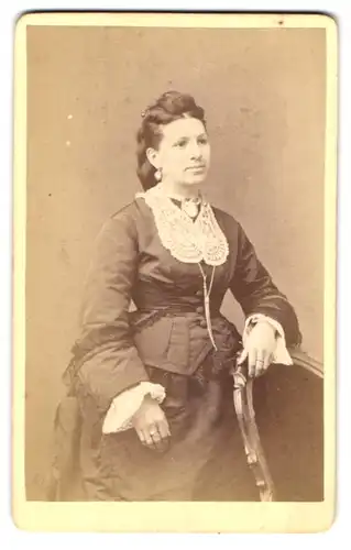 Fotografie H. Kopp, Baden-Baden, Schillerstr. 1, Junge Dame im taillierten schwarzen Kleid mit Brosche und Ohrringen