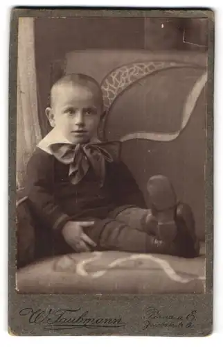 Fotografie W. Taubmann, Pirna a. E., Kind mit grosser Schleife auf einem Sessel