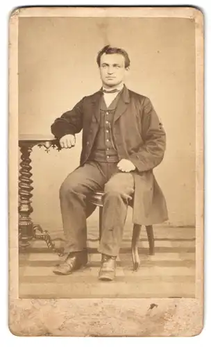 Fotografie Nic. Leyendecker, Berncastel, Mann mit Mantel an einem Tisch