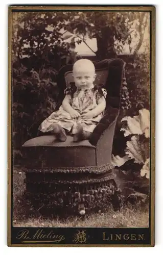 Fotografie B. Mieling, Lingen, Niedlicher Junge im Kleid auf einem Sessel im Garten