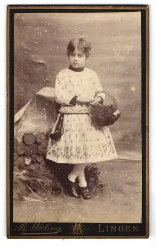 Fotografie B. Mieling, Lingen, Mädchen im Kleid mit einem Korb vor Holzdekoration