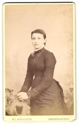 Fotografie R. I. Houlson, Abergavenny, Junge schöne Dame im schwarzen taillierten Kleid mit Ansteckblume