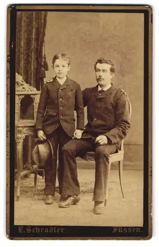 Fotografie L. Schradler, Füssen, Vater mit Schnauzbart hat liebevoll die Hand auf die Schulter seines Sohnes gelegt