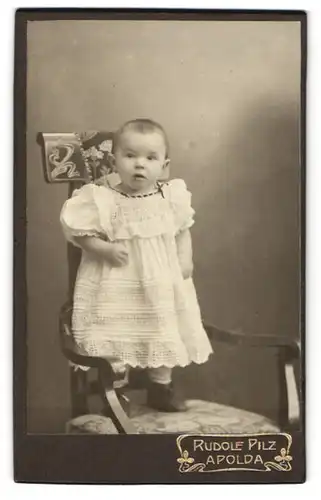 Fotografie Rudolf Pilz, Apolda, Ackerwandstr. 34, Zweijähriges Mädchen steht im Kleid auf einem Stuhl