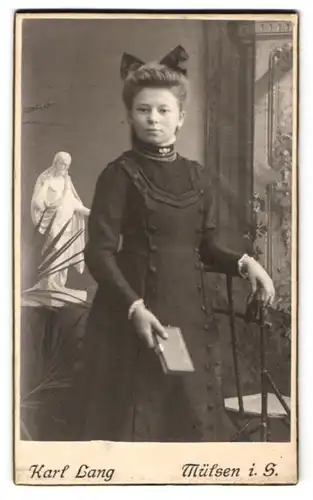 Fotografie Karl Lang, Mülsen i. S., Hübsches junges Mädchen steht kerzengerade und mit Schleife im Haar vor d. Kamera