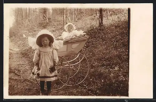 Foto-AK Kleines süsses Mädchen mit mürrischer Miene vor dem Kinderwagen mit ihrem Geschwisterchen