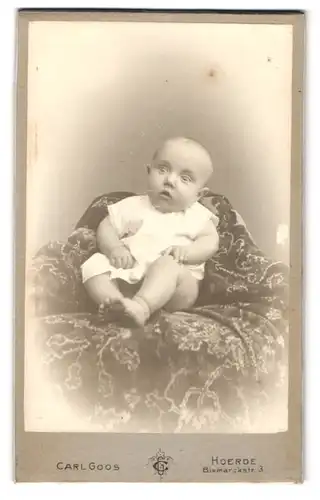Fotografie Carl Goos, Hoerde, Bismarckstr. 3, Erstauntes Baby im weissen Oberteil auf einer Zierdecke